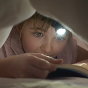 boy under covers reading with headlamp