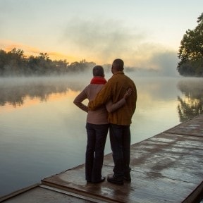 Retired couple standing by lake. 