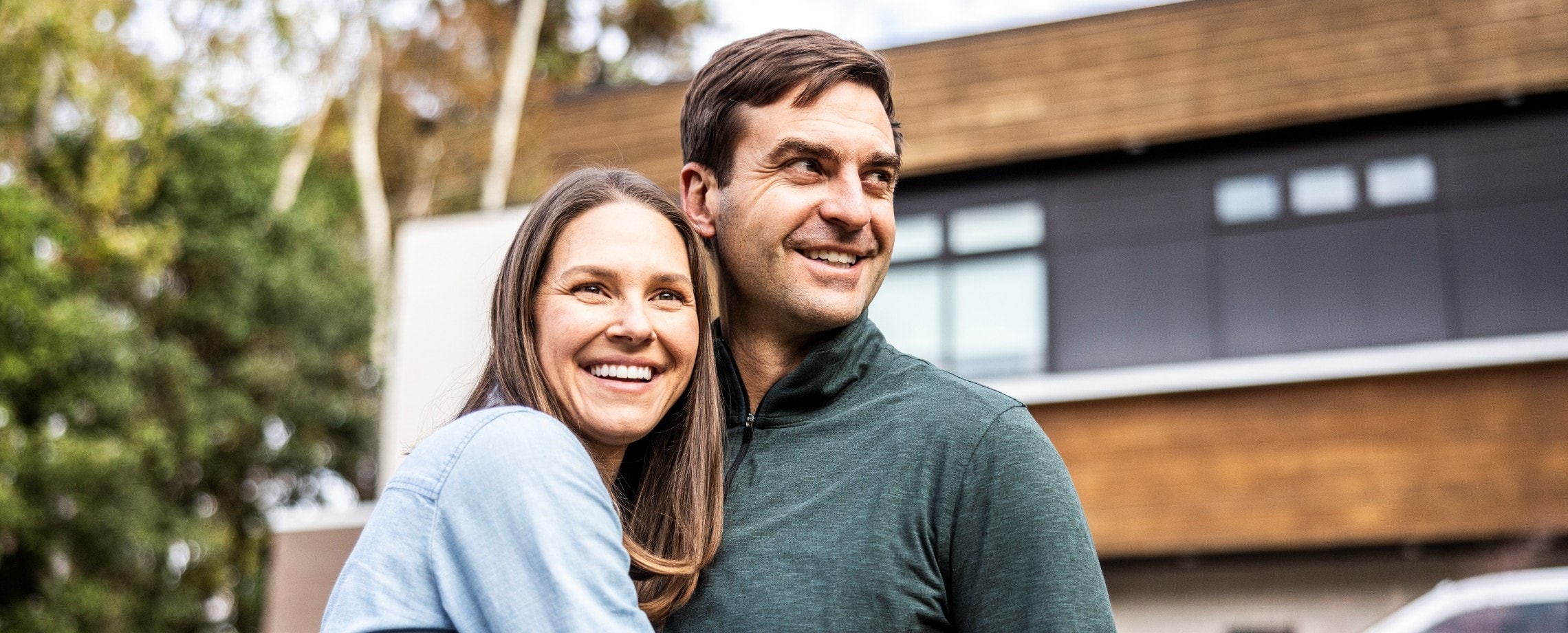 Couple hugging in front of house.