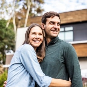 Couple hugging in front of house.