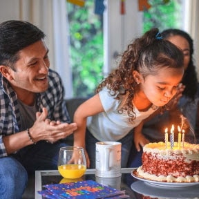 Father watching daughter blow out candles.