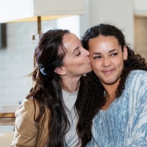 mom kissing college-age daughter
