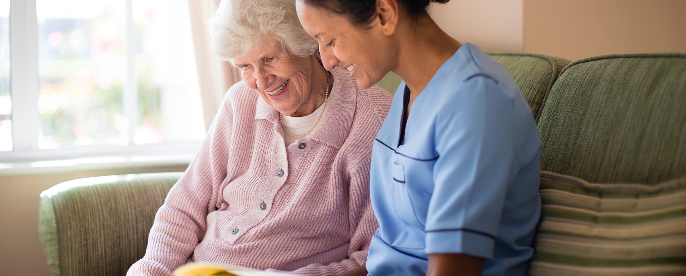 White haired older woman sitting with younger woman in nurse's blue blouse
