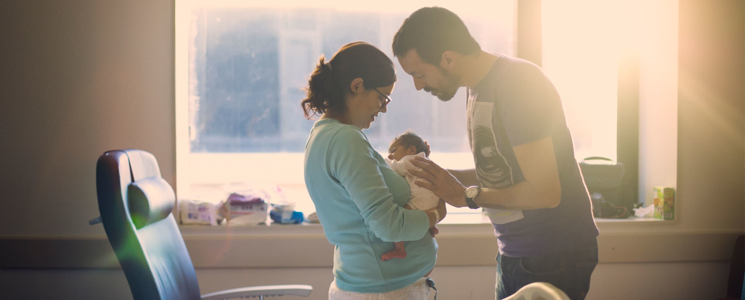 Young mother holding a newborn baby with father looking on with his hands on the baby