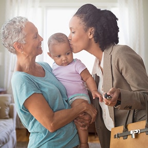 African-American grandmother holding grandbaby; the mother is kissing the baby before leaving for work