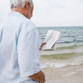 Older man looking at a newspaper while at the beach