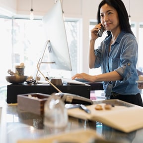 Asian woman standing at computer while talking on the phone