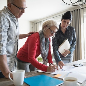 Older couple signing a document with a woman assisting them