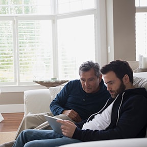Father and son studying laptop on couch