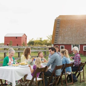 Multigenerational family eating outside at a long table by the barn