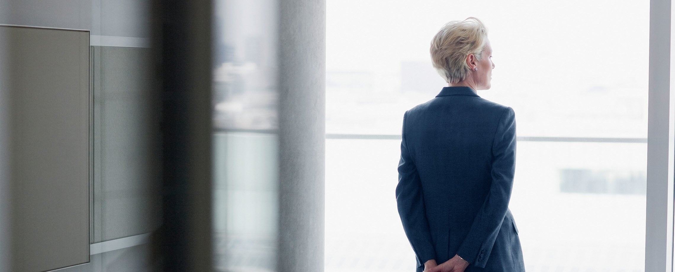 Short-haired businesswoman looking out a floor-to-ceiling window