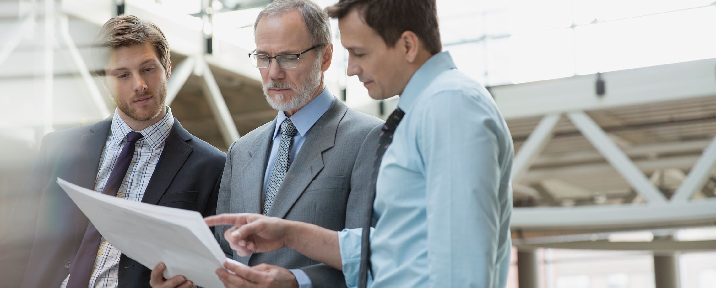 Three Caucasian men of varying ages in office attire looking down at plans