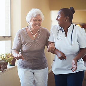 African-American nurse helping walking arm in arm with an older Caucasian woman