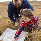 Father and young child in a field crouched down inspecting map on the ground