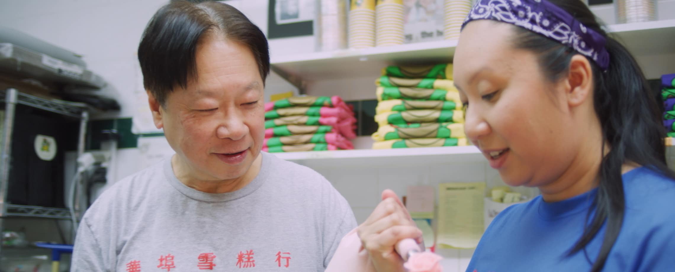 Asian father looking on as his daughter decorates a cake in their store