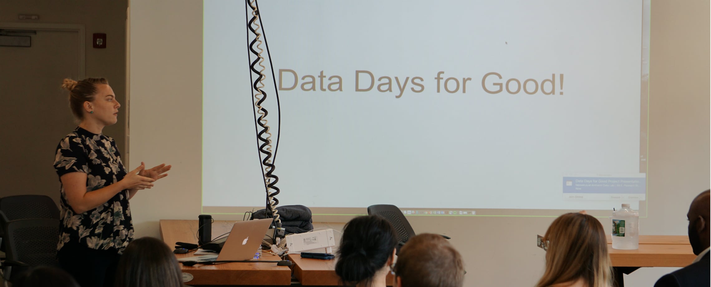 Female teacher making presentation with 'Data Days for Good!' projected on wall