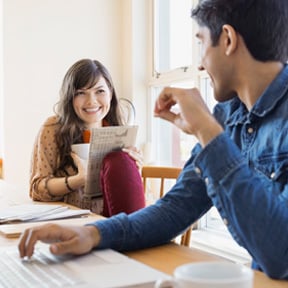 Young couple with coffee cups, newspaper and laptop in kitchen
