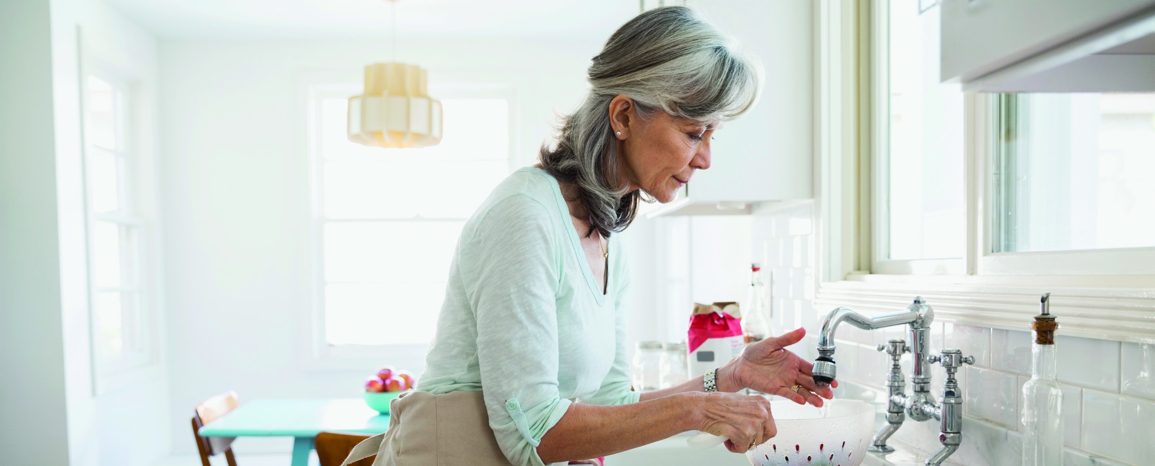 Retirement aged Caucasian woman at kitchen sink rinsing something in colander