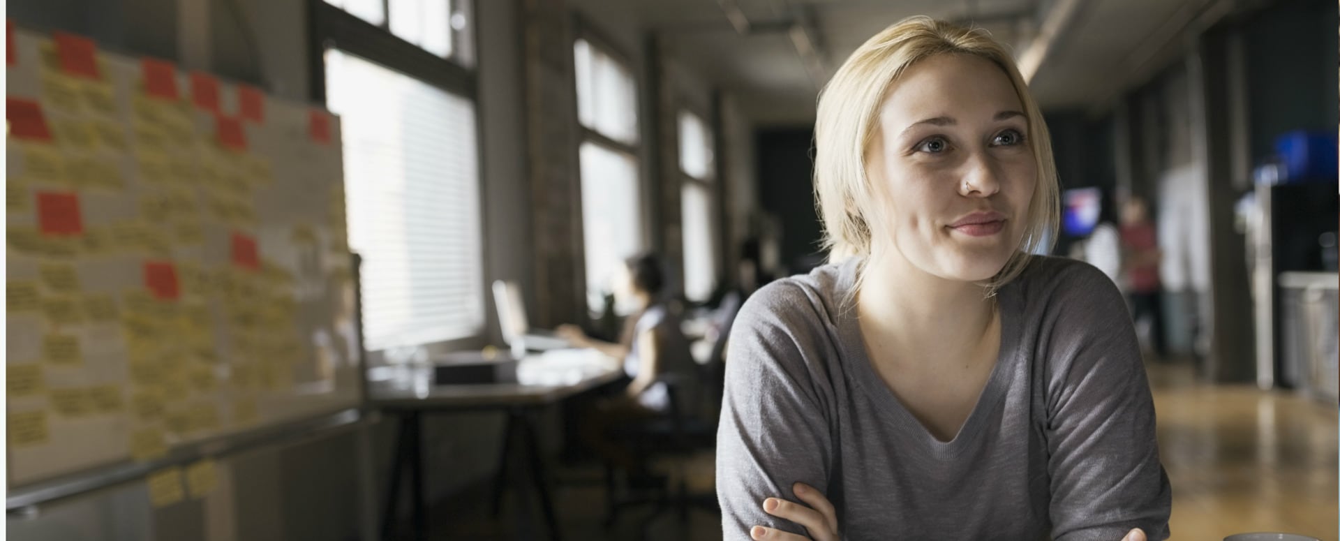 Young Caucasion female in an office setting, smiling, pondering a bright future