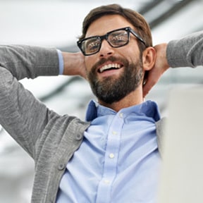 Bearded office worker sitting back with his hands behind his head and smiling