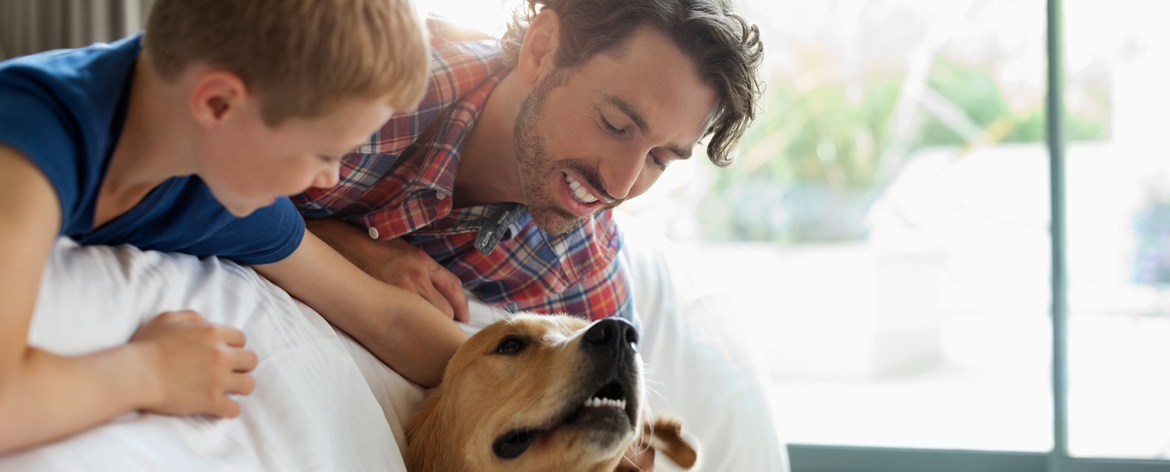 Man and son lying on bed petting their dog