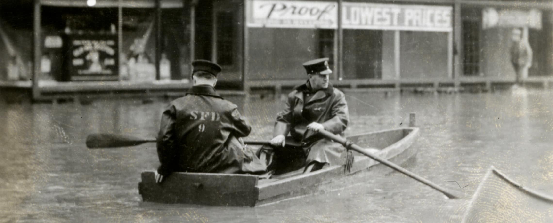 Two Springfield, Massachusetts firefighters rowing a boat down a city street after a 1936 flood