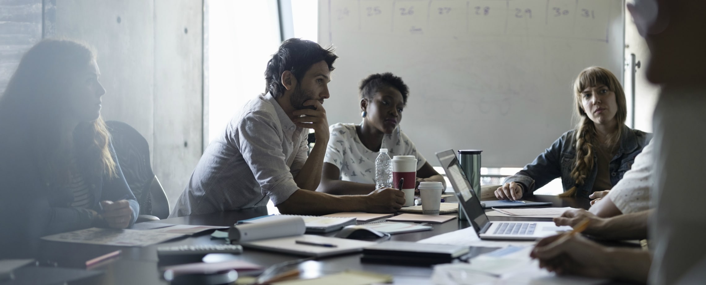 Young office workers of various races sitting around messy conference table