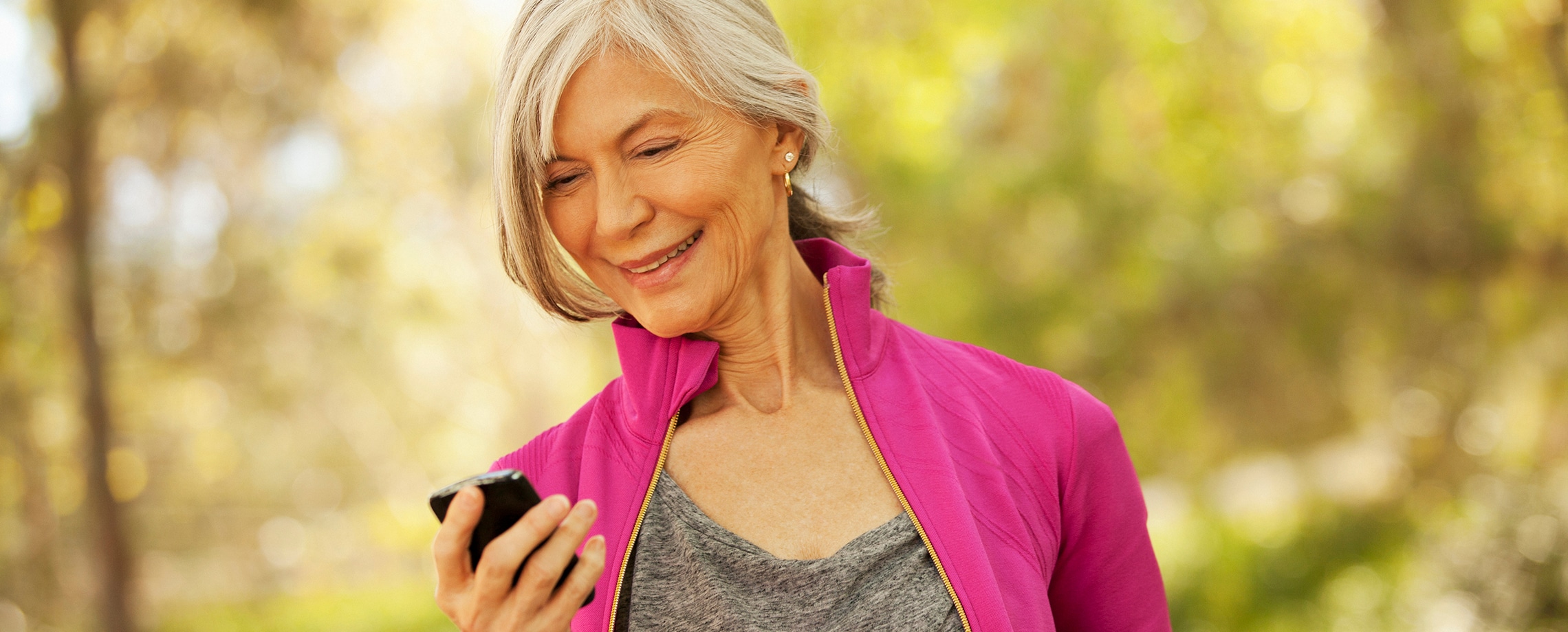 Older Caucasian woman in bright magenta jacket looking at BlackBerry