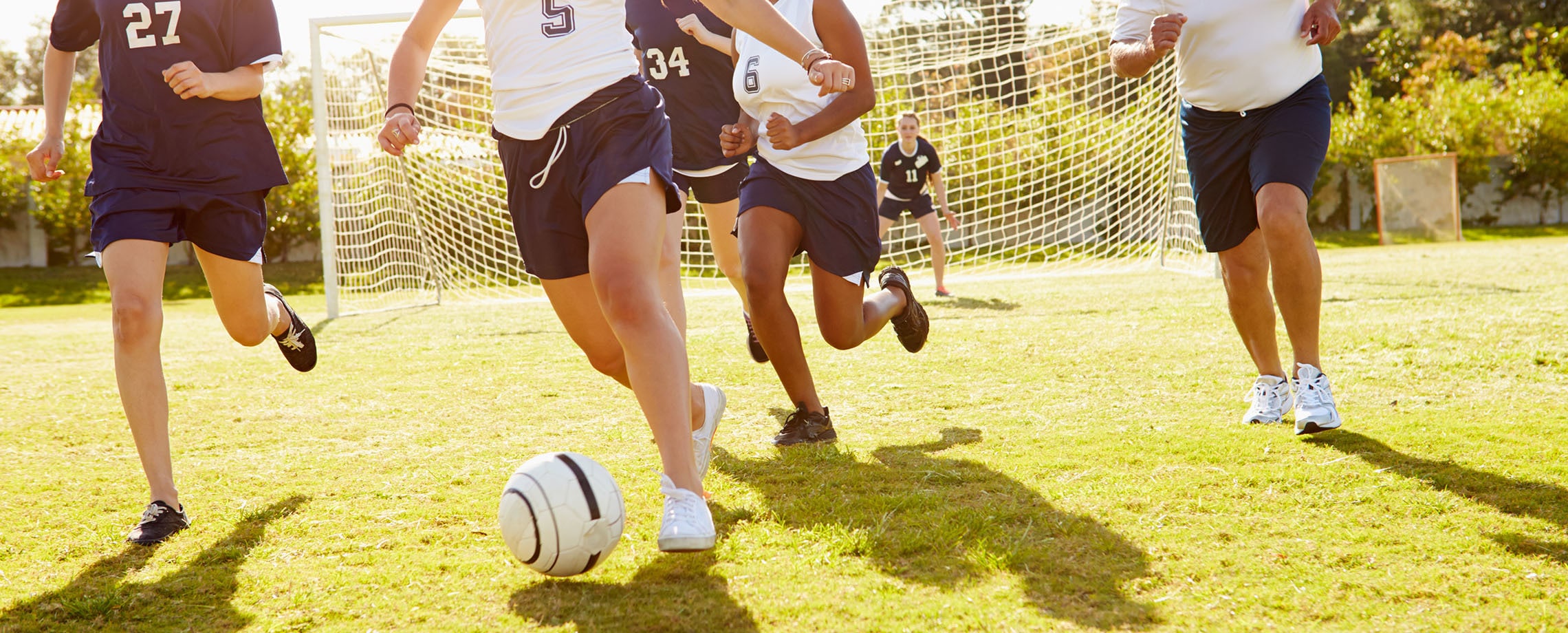 Young women playing soccer as older man with whistle runs with them