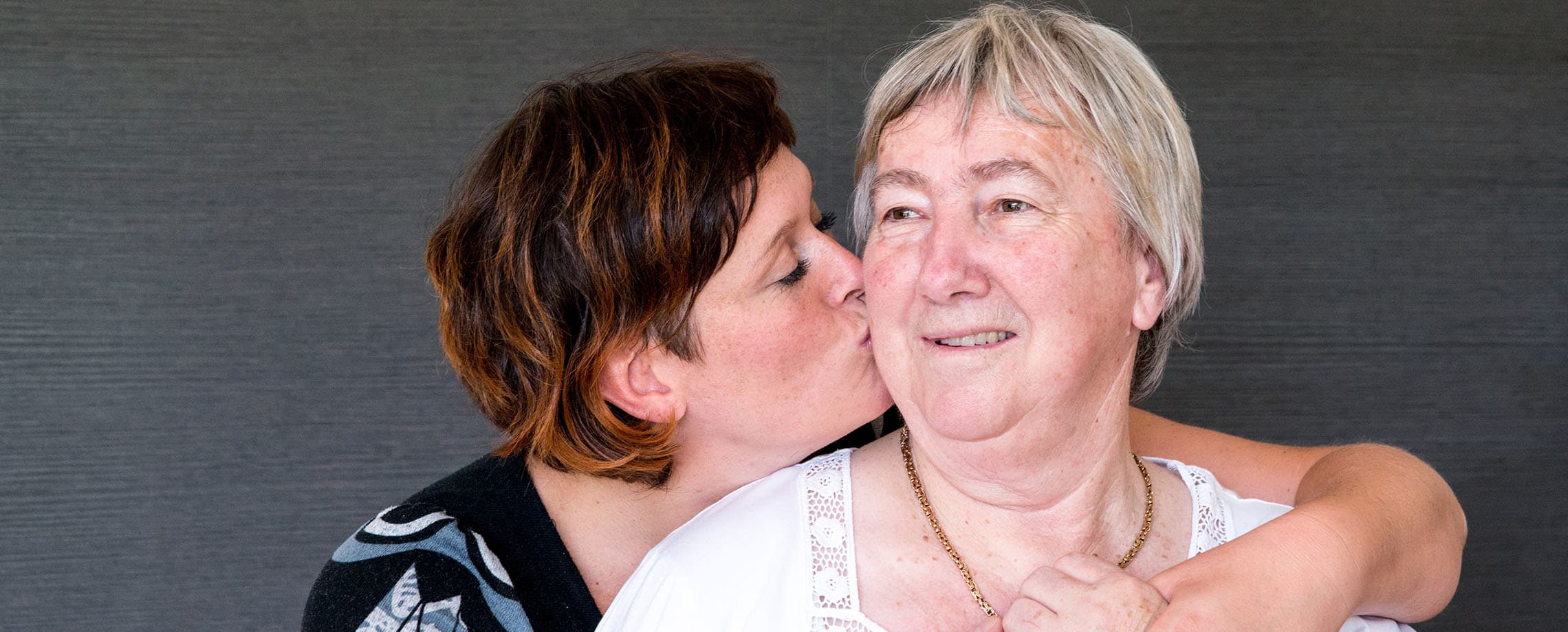 Young woman with arm around her mother's shoulder giving her a kiss