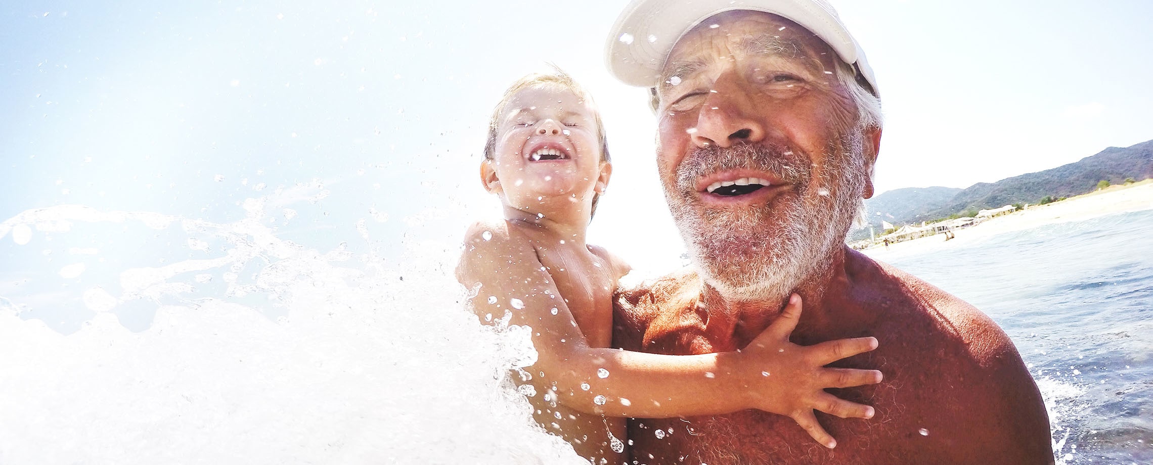 Close up Bearded old man frolicking with grandson in surf