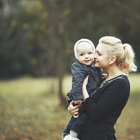 Blond woman with ponytail holding a baby in fall clothes