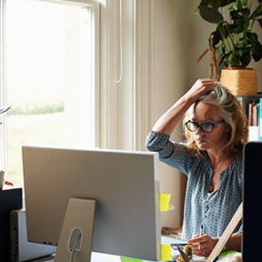 Woman sitting in front of computer next to window; she is clutching her hair with one hand
