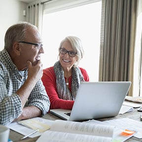 Retirement aged Caucasian couple looking at laptop with papers spread on table