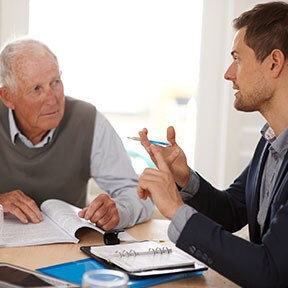 Books and pads on table with younger man explaining something to an older gentleman