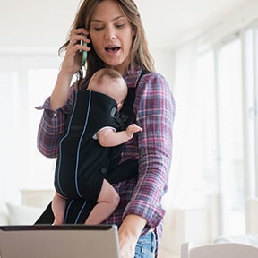 Young with baby in carrier on chest talking on phone