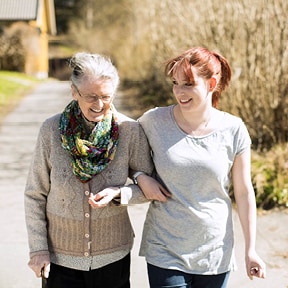 Older woman with cane walking arm-in-arm with younger woman