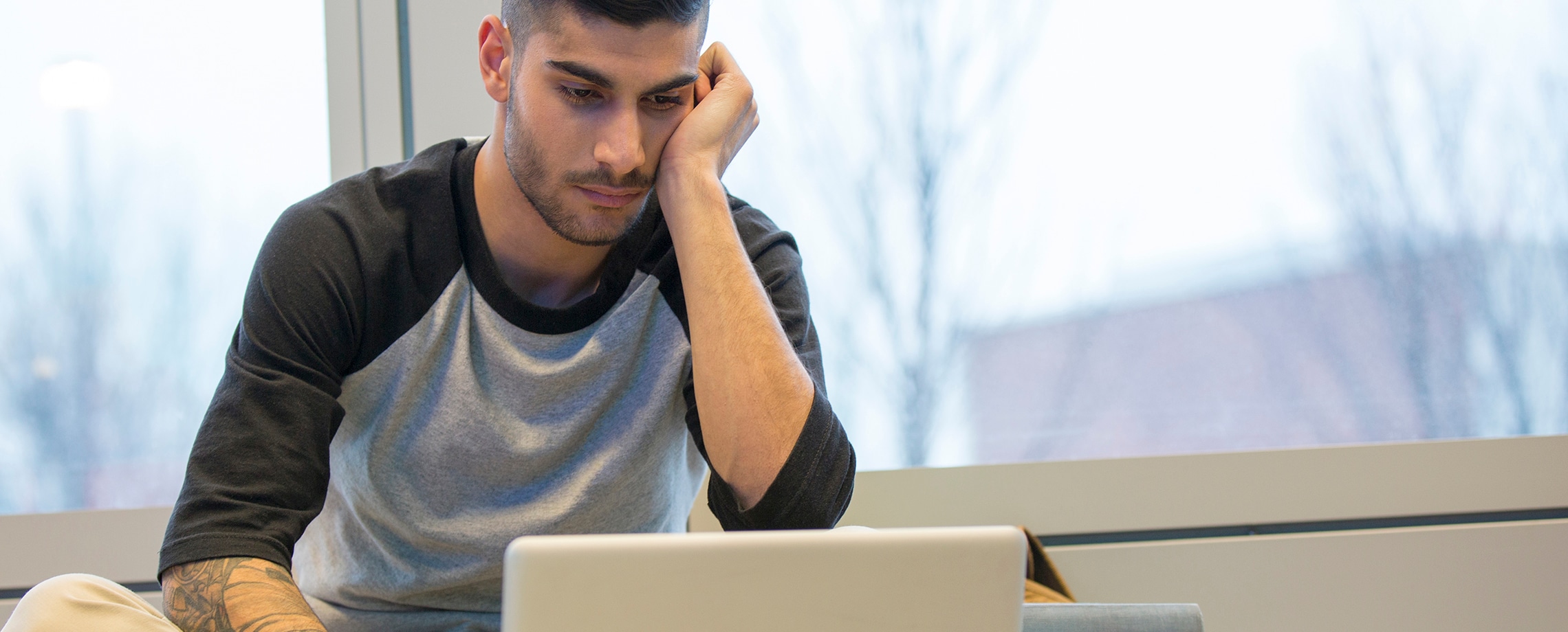 Young man looking at laptop, downcast, head supported by his hand