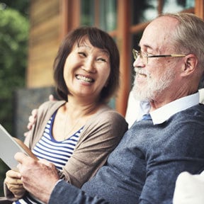 Older couple of two races sitting on front porch looking at papers and smiling