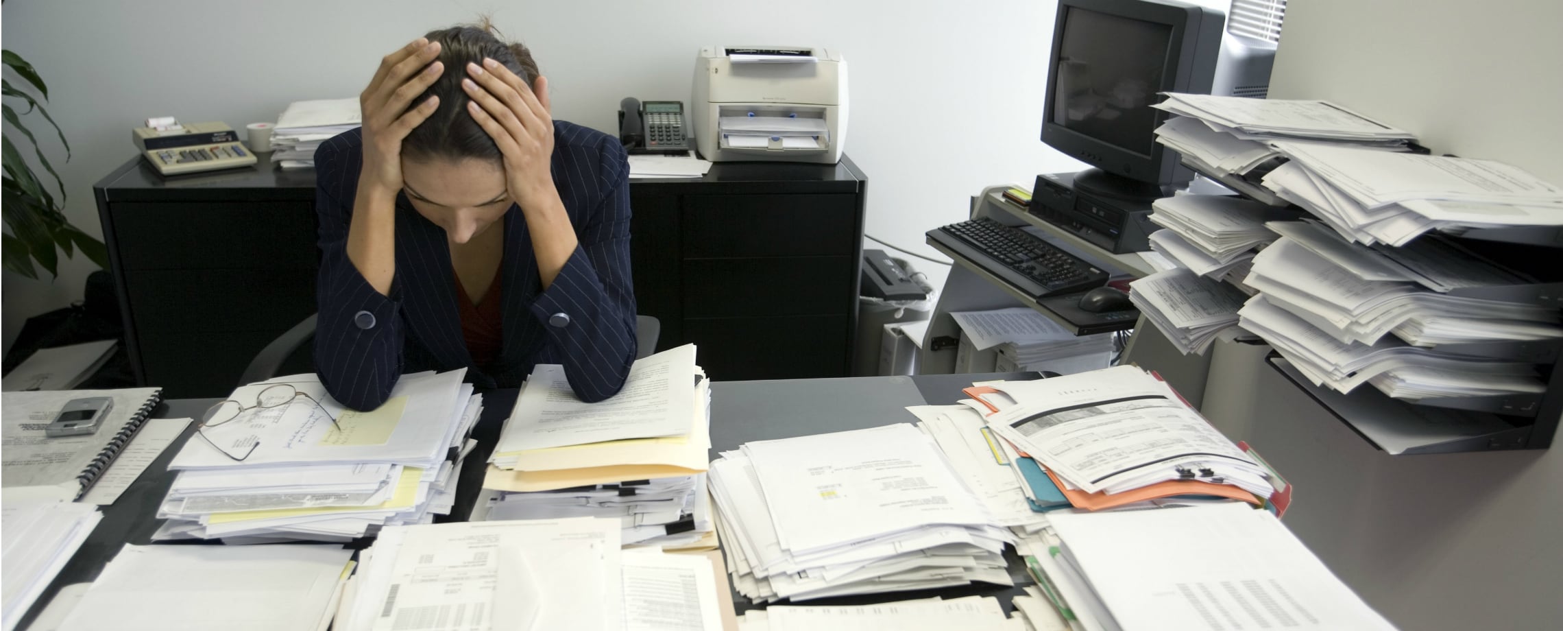 Woman with her hands on her head looking down at a desk cluttered with papers