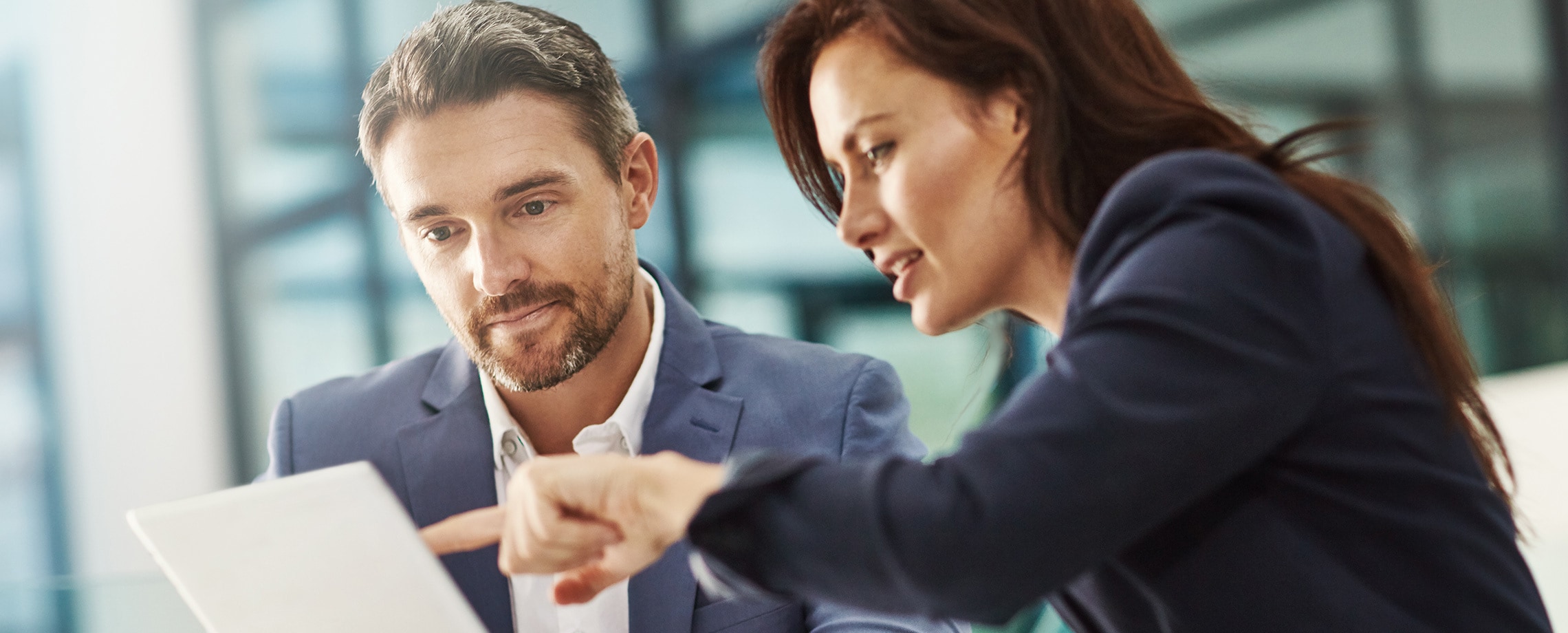 Caucasian man with beard looking at female coworker pointing something out on paper