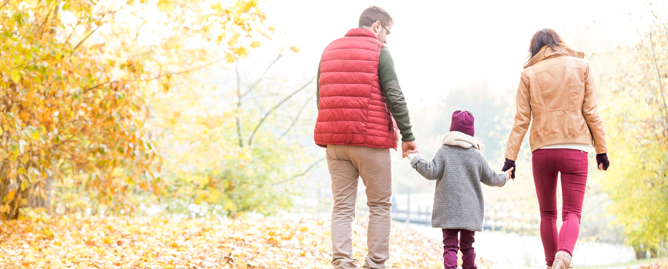 Young girl holding one hand of each parent as they walk outside in autumn