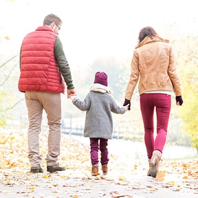 Distant view of young girl holding one hand of each parent as they walk outside in autumn