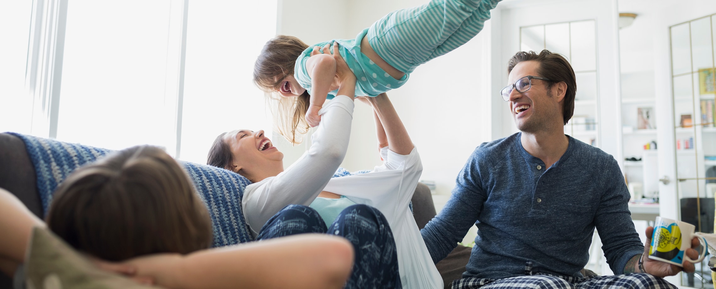Caucasian mother sitting on couch holding young daughter in the air while father looks on