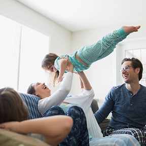 Caucasian mother sitting on couch holding young daughter in the air while father looks on