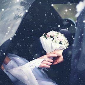 Close up of man and woman's hands holding bouquet while it's snowing