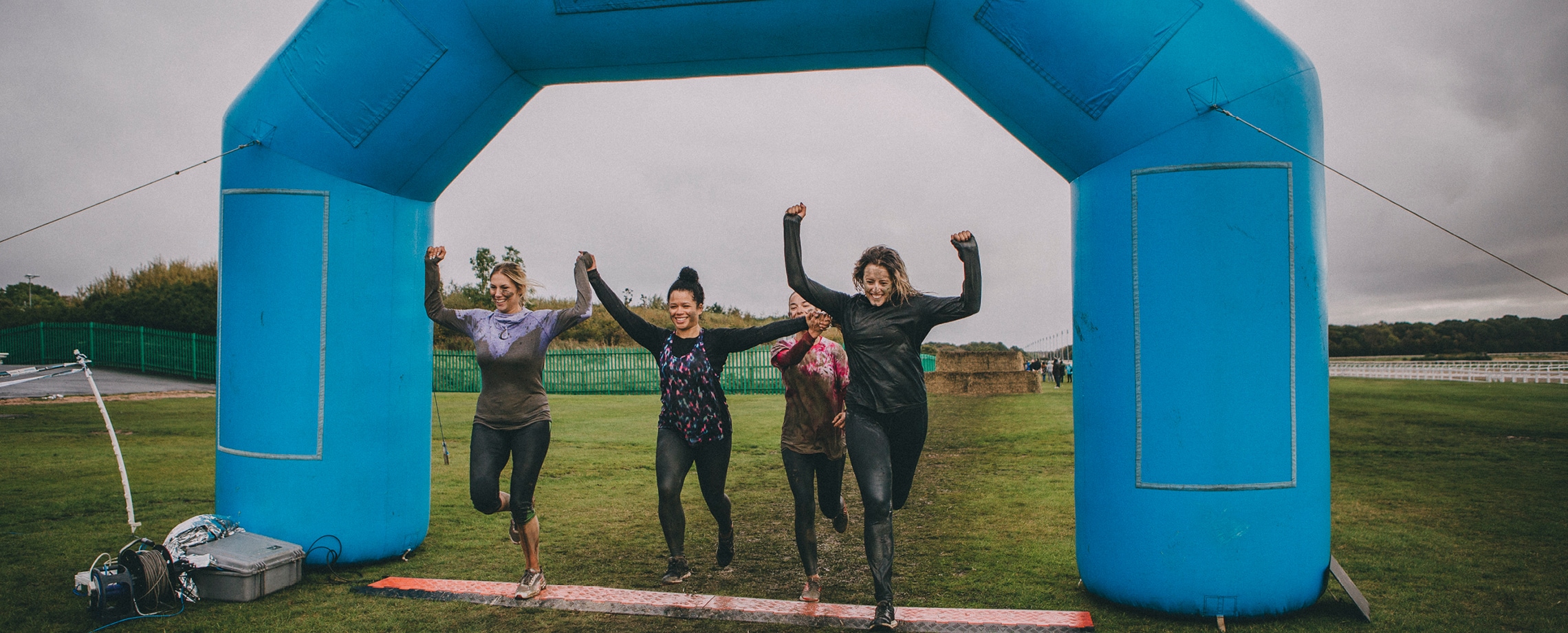 Close up of four young women crossing the finish line of a mud run type race