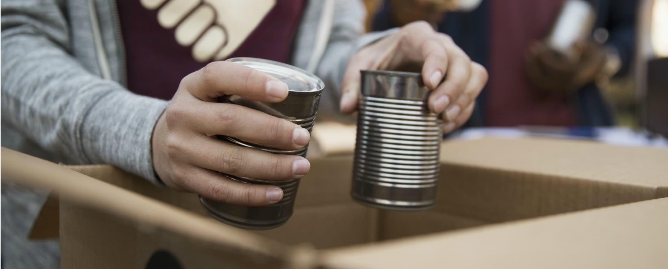 Close up of person's hands packing unlabeled food cans into a box