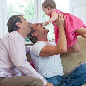 Two Caucasian men playing with a baby in a pink dress