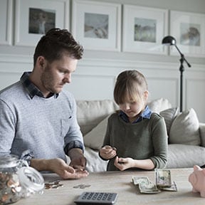Young girl and her father counting her savings at a table